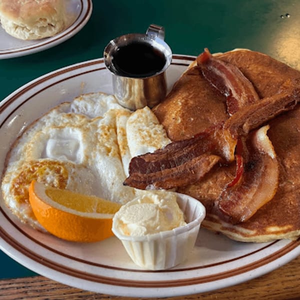 A Mother Hubbard's breakfast plate with pancakes, bacon, fried eggs, an orange slice, and butter.