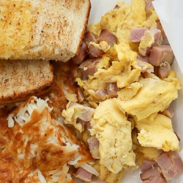 A breakfast plate with scrambled eggs, diced ham, crispy hash browns, and two slices of toast.