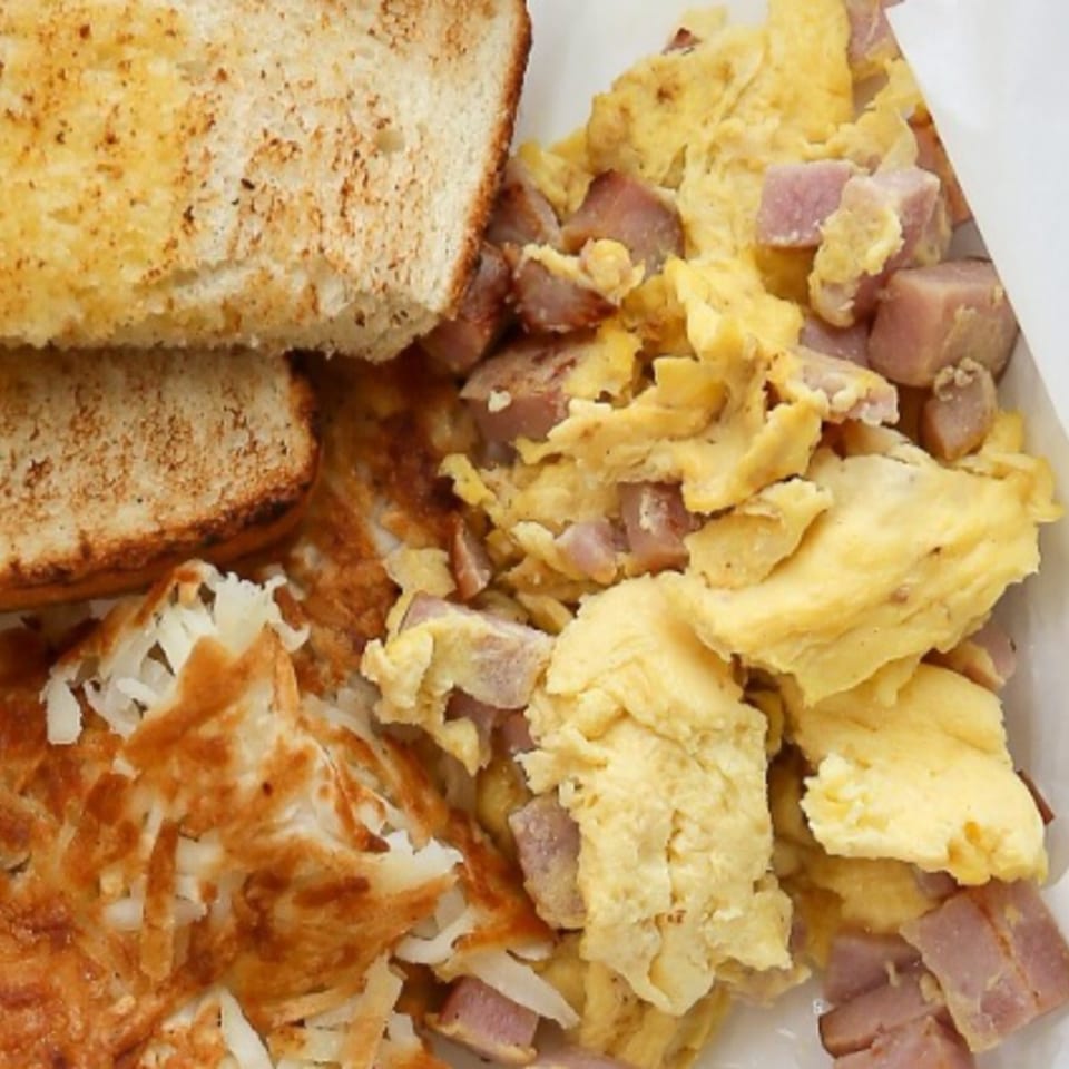 A breakfast plate with scrambled eggs, diced ham, crispy hash browns, and two slices of toast.