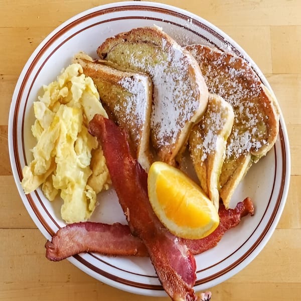 Mother Hubbard's breakfast plate with French toast, scrambled eggs, bacon, and an orange slice.