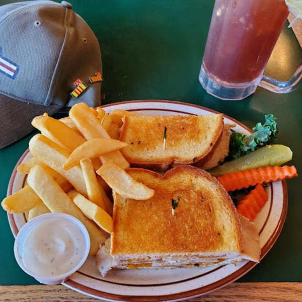 A grilled cheese sandwich with fries, pickle, carrots, and a drink on a green table.