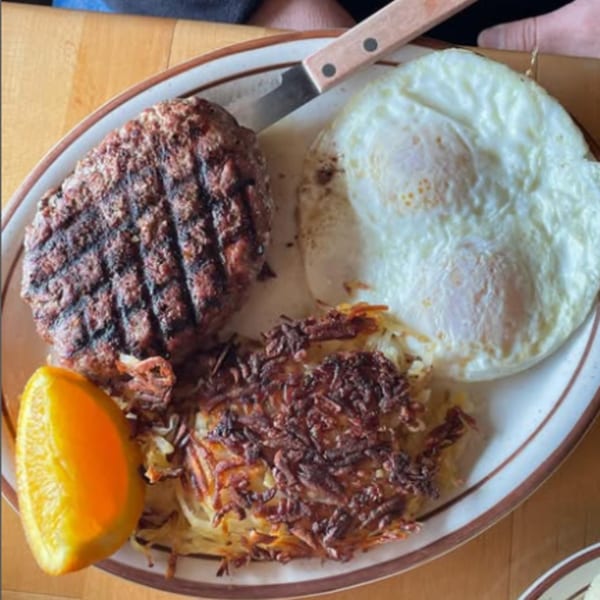 Mother Hubbard's breakfast plate with grilled hamburger patty, fried eggs, hash browns, and an orange slice.