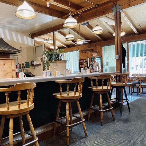 Interior of Mother Hubbard's Restaurant, showing a long counter with stools and a family in the background.