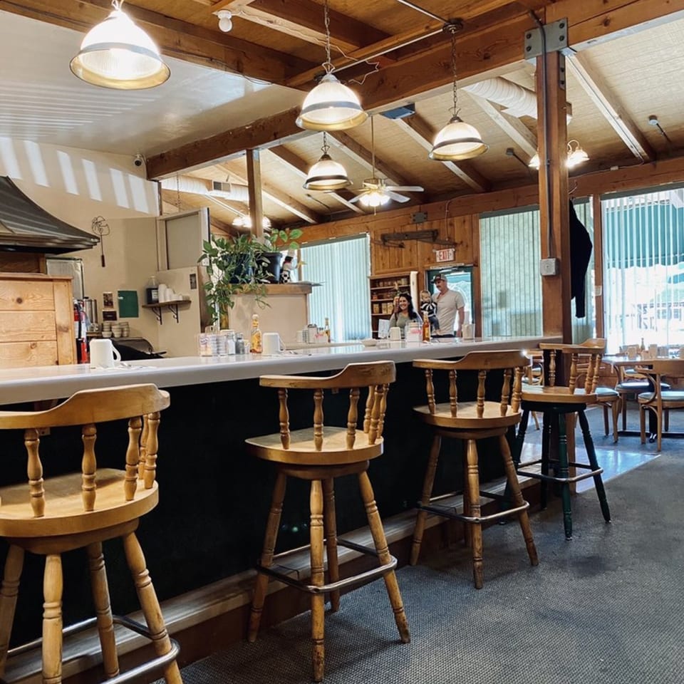 Interior of Mother Hubbard's Restaurant, showing a long counter with stools and a family in the background.