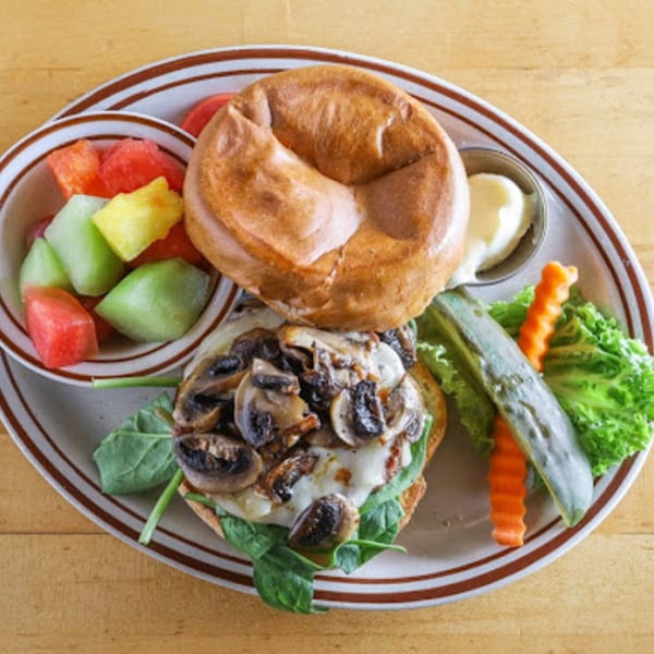 Mushroom and cheese sandwich with a side of fruit salad, lettuce, and a pickle.