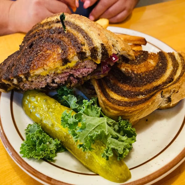 A Mother Hubbard's patty melt on marbled rye with a pickle spear and kale garnish.
